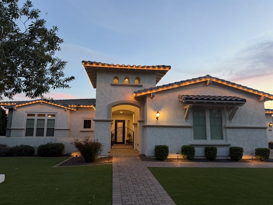 A stucco home at dusk with warm white lights tracing every roofline