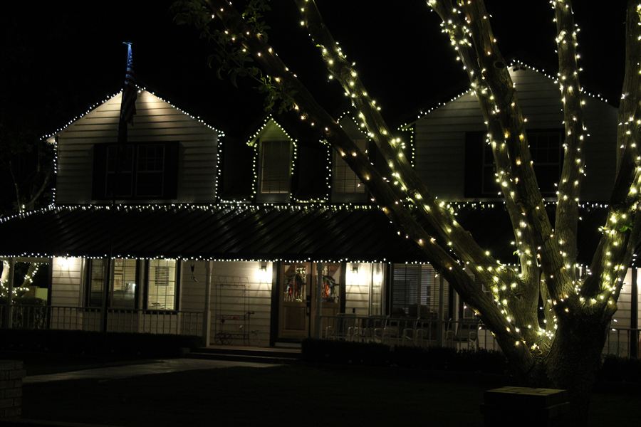 Two-story home with a lit roofline and a wrapped tree in the foreground